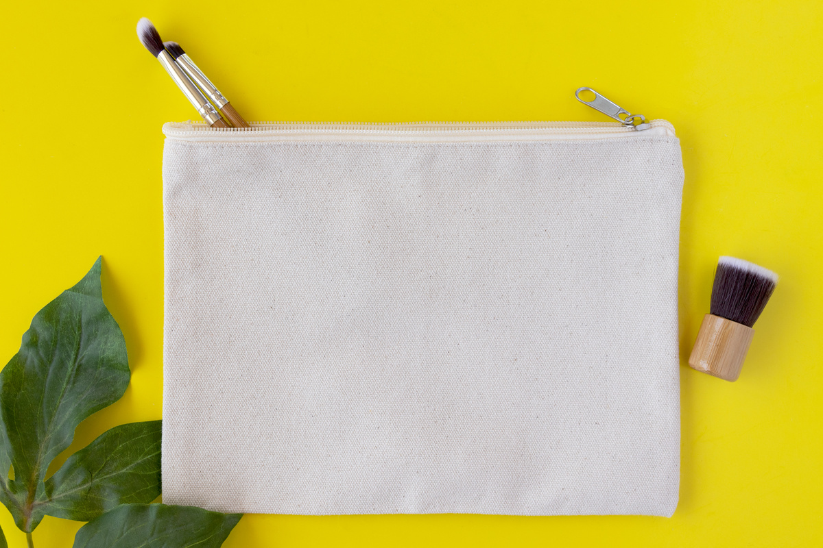 Blank canvas makeup bag on a bright yellow background with green leaves - eco makeup bag concept mockup